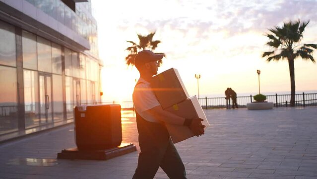a male loader in uniform walks with a box in his hands at sunset
