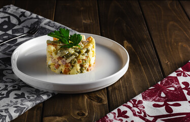 Traditional russian salad Olivier from boiled vegetables and sausage with mayonnaise in bowl. Russian New Year or Christmas salad on wooden background with copy space.