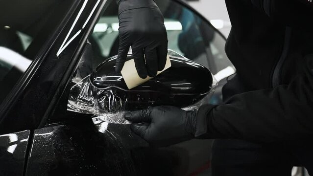 Close video shot of paint protection film being put onto a car mirror by a pair of gloved hands. High quality 4k footage