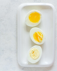 Halves of a cracked boiled egg with a liquid, semi-liquid and dry yolk on a white plate on a light concrete background