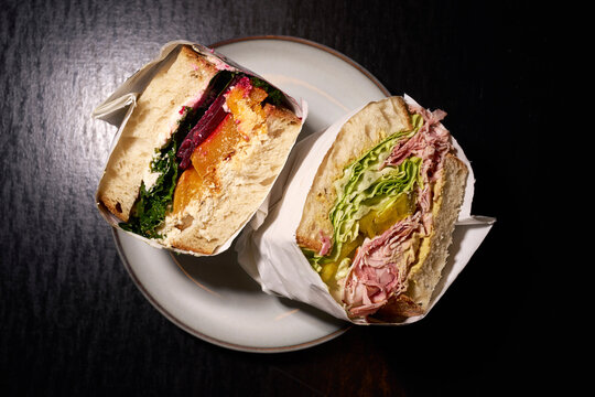 Still life gourmet sandwich halves wrapped in paper on plate
