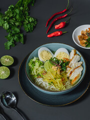 A bowl of noodles with eggs, slice of chicken and vegetable as  a background