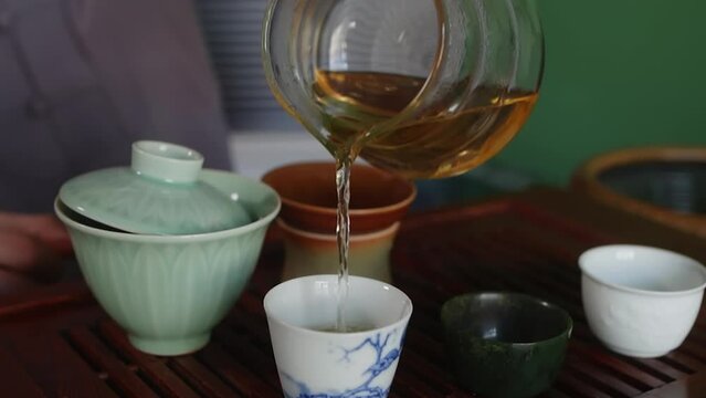 Tea master pouring fresh brewing tea to bowls on wooden table chaban, hands close-up. Professional traditional chinese tea ceremony concept. Preparing serving hot beverage, drink for tea drinking.