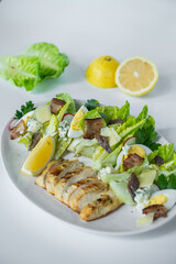 A bowl of salad with shrimps and salmon with a bowl of potato chips, lemon and  salad dressing