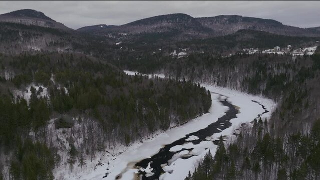 Aerial scenic drone pan backwards Canadian  wilderness mid winter near north Quebec Stoneham Ski Resort of frozen over Sautaurski River with cozy cabin and chalets