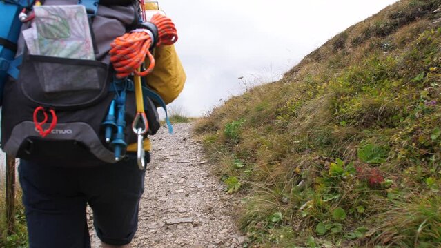 Young man hiker hiking on mountain dirt road with cloudy sky and fog. Yellow jacket, backpack, black beard and beanie. Traveling Dolomites, Italy.