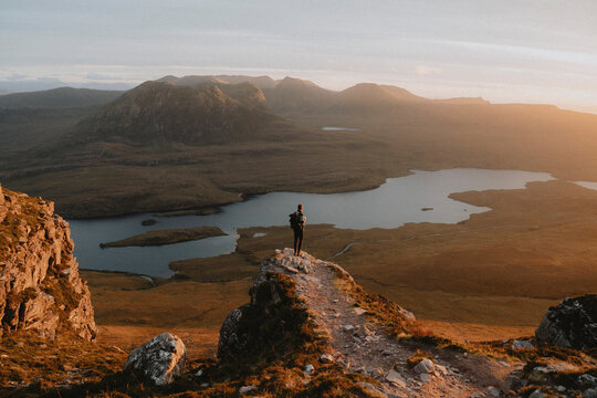 Hiker standing on mountain overlooking idyllic sunset view, Assynt, Sutherland, Scotland
