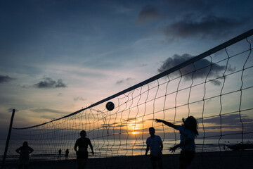 Silhouette of friends playing beach volleyball at sunset