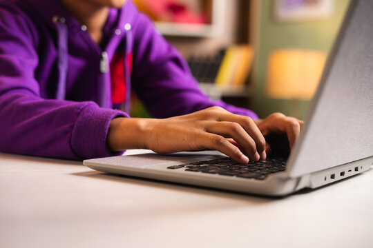 Close up shot of indian kid hands using laptop in front of notebook at home - concept of technology, learning and development