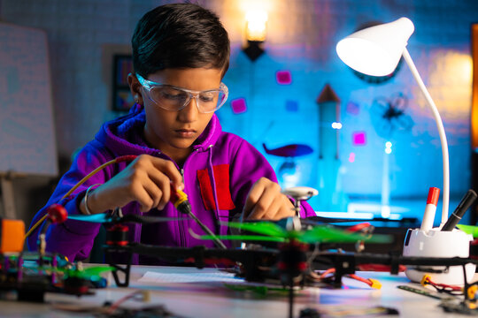 Intelligent serious indian kid busy making drone connections by soldering at home during night - concept of genius, smart kid and innovation.