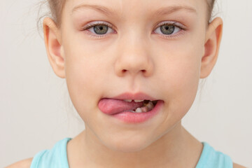 Child face with tongue out to left side cropped head caucasian little girl of 6 7 years on grey background