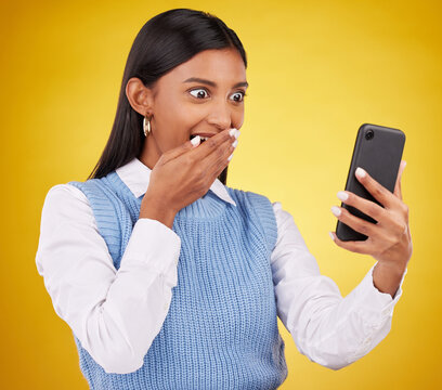 Wow, surprise and woman with phone in studio space reading text or email on yellow background. Technology, communication and good news, happy Indian girl with social media gossip or online content.