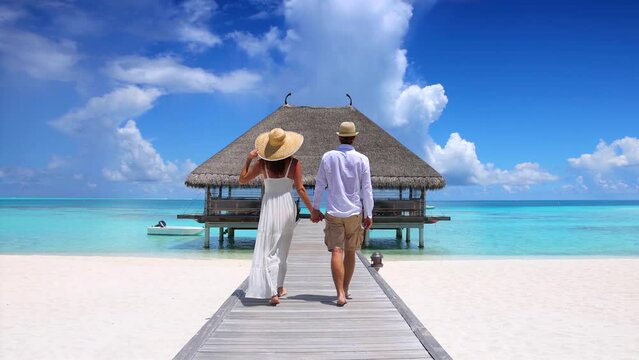 A happy holiday couple in white summer clothing walks down a wooden pier  in the Maldives islands, Indian Ocean