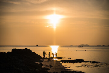 Silhouette of four children playing on the beach with sunset background and boats.