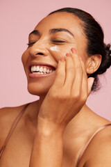 Smiling woman applying moisturizer cream on face