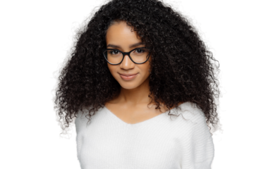 Close up shot of dark skinned female has satisfied expression, bushy curly hair, wears spectacles and white jumper, looks straightly at camera, models over grey background. Natural beauty concept