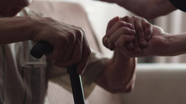 an adult son helps an elderly father, who is leaning on a walking stick, to get up and walk. selective focus. rehabilitation, old man recovery, be healthy