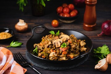Green lentil stew with vegetables and mushrooms on a black plate on a dark wooden background. Vegan recipes, lenten menu, healthy food, diet.