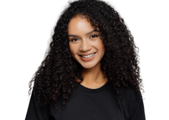 Optimistic curly young woman with gentle smile, looks positively at camera, wears casual black clothes, isolated on grey background, listens interesting story or funny anecdote. Emotions concept