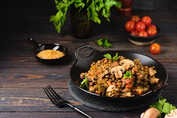 Green lentil stew with vegetables and mushrooms on a black plate on a dark wooden background. Vegan recipes, lenten menu, healthy food, diet.
