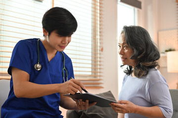 Young male doctor pointing at digital tablet, sharing health tests laboratory results to senior female patient