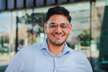 close up portrait of hispanic young entrepreneur smiling and looking at camera at workspace. Front...