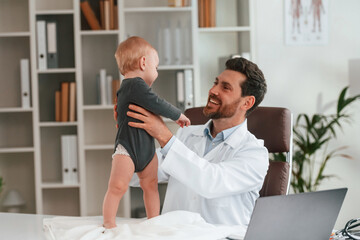 Holding boy in hands. Doctor with little baby is working in the cabinet