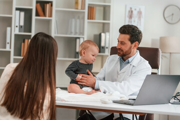 Obraz premium Having consultation. With baby and mother. Doctor in formal clothes is working in the cabinet