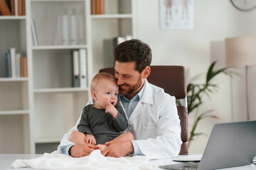 Friendly positive doctor with little baby is working in the cabinet