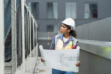 Female engineer worker working, holding blueprint and inspecting structure of building at rooftop...