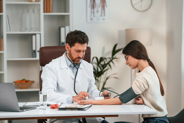 Measuring blood pressure. With woman. Doctor in formal clothes is working in the cabinet