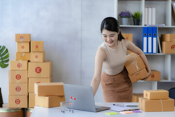 Charming asian woman starting a small business, SME entrepreneur, distribution warehouse with post box. owner's small home office Online marketing and product packaging and home delivery services.