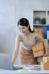 Attractive Asian woman starting a small business, SME entrepreneur with post box owner's small home office Online marketing and product packaging and home delivery services vertical image