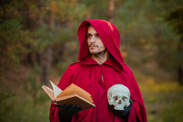 A sorcerer in red clothes with a skull and a book in his hands reads a spell. Medieval monk reads a...