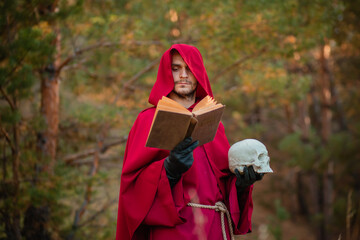 A sorcerer in red clothes with a skull and a book in his hands reads a spell. Medieval monk reads a...