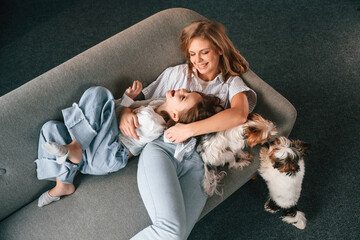 Positive emotions, relaxing on the sofa. Mother with her daughter and with two cute dogs is in...