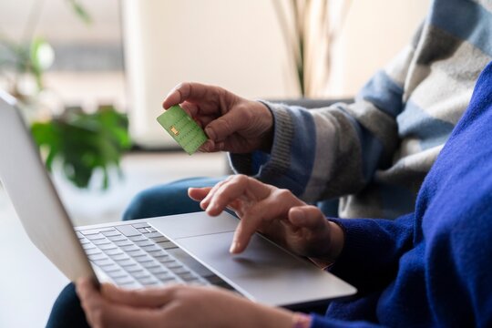 Crop anonymous women using laptop while paying online with credit card for purchases on internet remotely from home