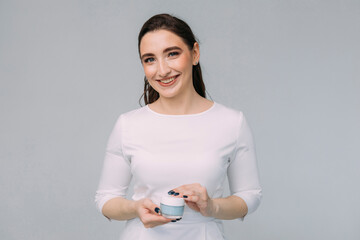 young girl doctor in a white dress holds a moisturizer in her hands, studio photo
