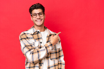 Young caucasian handsome man isolated on red background pointing finger to the side