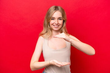 Young English woman isolated on red background holding copyspace imaginary on the palm to insert an ad