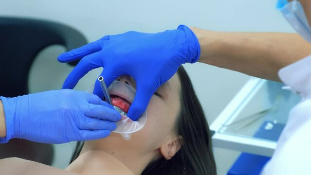 Orthodontist is fixing metal part on woman's patient teeth preparing to condylography. Examination and treatment of mandibular joints. Orthodontology treatment and cure concept. Dentistry and clinic.