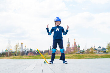 happy child, schoolboy in a protective purple helmet, protection on elbows and knees stands with a skateboard. a boy in the Zaryadye park, in the distance you can see the Moscow Kremlin, St. Basil's C