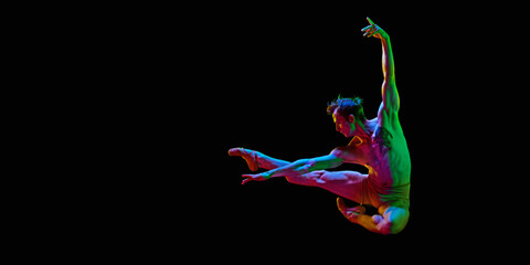 Banner with one young man, ballet dancer jumping in air over dark studio background with neon light. Copy space for ad, text. Freedom