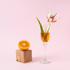 Slices orange with glass and flower on pink background. Creative concept.