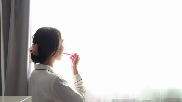窓の外を眺めながら歯磨きをする女性