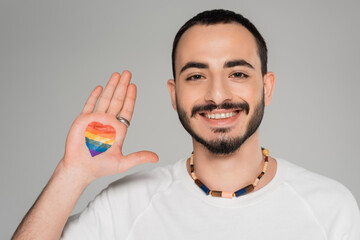 Cheerful young homosexual man with lgbt flag on hand looking at camera isolated on grey.