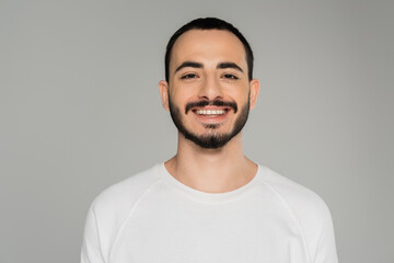 Portrait of smiling gay man in white t-shirt looking at camera isolated on grey.