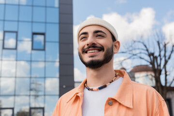 Portrait of positive and stylish gay man standing on blurred urban street.