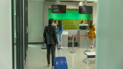 Female business traveler caries a blue small suitcase to check in counter before taking flight at an airport. Lady walks with her carry on bag to the gate getting her journey.