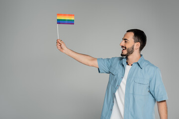 Side view of cheerful homosexual man holding lgbt flag and looking away isolated on grey.